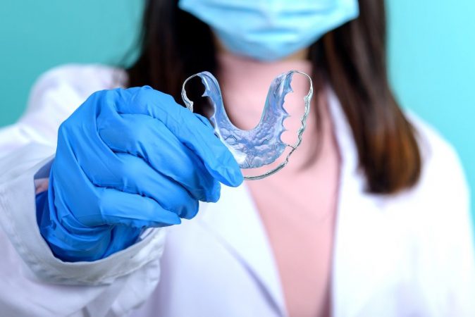 Dentist woman holding orthodontic retainer on blue screen background. Dental care and healthy teeth.